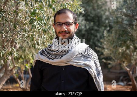 portrait pour homme portant keffiyeh dans le champ d'oliviers avec fond noir et chemises noires également avec expression faciale sourire Banque D'Images