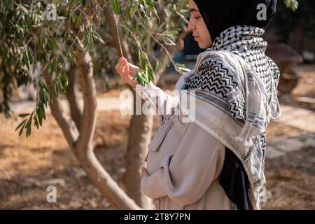 Femelle tenant une branche d'olivier tout en portant du keffiyeh palestinien dans le champ Banque D'Images