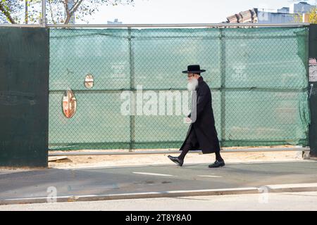 Une scène de rue Williamsburg, Brooklyn. Un homme plus âgé, probablement un rabbin Satmar, portant de hautes chaussettes noires passe devant un chantier de construction sur Lee Avenue. Banque D'Images