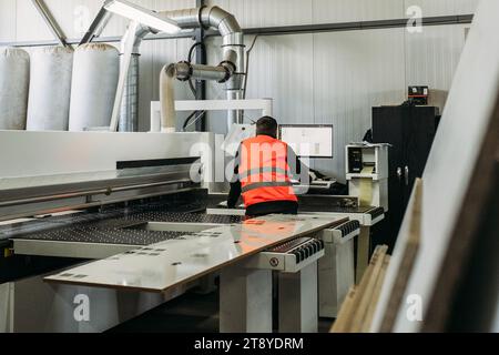 Un travailleur travaille sur une machine moderne pour couper des dalles de garnitures de meubles. Fabrication de meubles. Homme méconnaissable. Banque D'Images