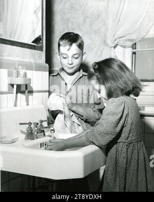 Tennessee, 1961 - les enfants d'une maison de ferme électrifiée dans le cadre du programme Tennessee Valley Authority (TVA) profitent des avantages de la plomberie intérieure. L'électricité, en plus de fournir de l'eau à l'intérieur et à l'extérieur, chauffe l'eau, fournit un meilleur éclairage, réfrigére le lait et d'autres aliments, et alimente une variété de machines agricoles économisant la main-d'œuvre. Tennessee, vers 1961. Photo de Tennessee Valley Authority/ NARA. Banque D'Images