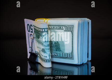 pile de billets de dollar collectés dans une bande élastique et un clip de papeterie, isolé sur un fond noir. Banque D'Images