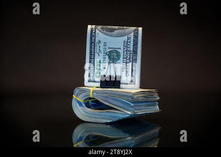 pile de billets de dollar collectés dans une bande élastique et un clip de papeterie, isolé sur un fond noir. Banque D'Images