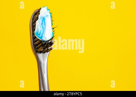 Brosse à dents avec poils noirs et pâte blanche et bleue sur fond jaune vif, soulignant l'hygiène dentaire Banque D'Images