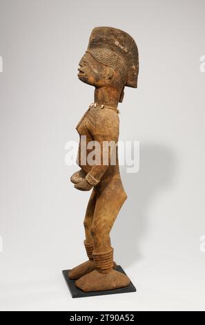 Figure de sanctuaire, c. 1900-1925, 32 3/16 x 7 7/8 x 7 7/8 po. (81,76 x 20 x 20 cm) (avec base attachée), Bois, coquilles de cowrie, ficelle, Nigeria, 20e siècle, tout au long du 20e siècle, le peuple Igbo a gardé des sanctuaires avec de grandes figures en bois représentant les divinités du village, qui ont offert protection et prospérité à la communauté. Comme cet exemple féminin, les personnages ont des coiffures élaborées, des scarifications sur le visage, la poitrine et le dos, et portent des ornements sculptés sur les bras et les jambes - toutes des marques de beauté et de haut rang dans la société traditionnelle Igbo. Banque D'Images