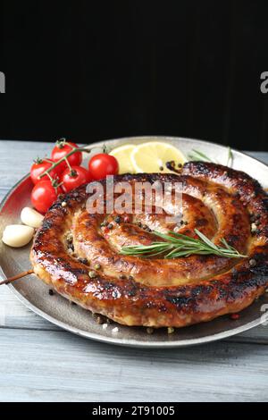 Délicieuse saucisse maison avec des épices, des tomates et du citron sur une table en bois gris clair sur fond noir Banque D'Images