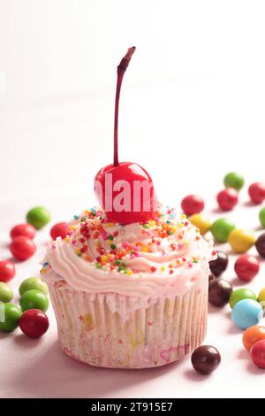 Cupcakes décorés de cerises et de saupoudrages colorés avec des bonbons ronds éparpillés sur le sol Banque D'Images