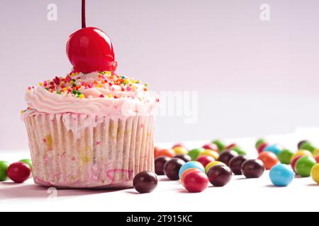 Cupcakes décorés de cerises et de saupoudrages colorés avec des bonbons ronds éparpillés sur le sol Banque D'Images