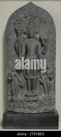 Vishnu avec Lakshmi et Sarasvati, période Pala, 11e siècle, 48 x 22 x 8 po. (121,92 x 55,88 x 20,32 cm), schiste gris, Inde, période Pala, 11e siècle, avec une assurance royale, le dieu hindou Vishnu se tient dans la posture de l'équilibre parfait, au sommet d'un lotus et au centre de l'univers. Vishnu est honoré comme le seigneur de la préservation, et avec son club et disque, maintient l'ordre sur la totalité de l'espace et du temps. Ici, il est flanqué par les déesses Laxmi, qui signifie richesse, et Sarastavi, qui joue d'un instrument à cordes et incarne la connaissance. Banque D'Images