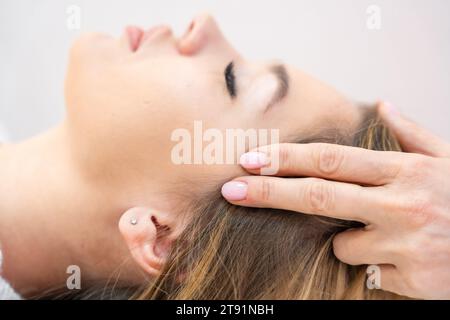 Vue rapprochée des mains de guérisseur exécutant par un ensemble légèrement touché de 32 points de barres d'accès sur la tête de jeune femme, stimulant les pensées de changement positif Banque D'Images