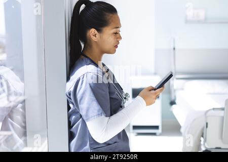 Médecin biracial portant des gommages à l'aide de smartphon à l'hôpital. Médecine, soins de santé, communication, travail et hôpital, intacts. Banque D'Images