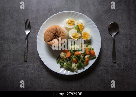Vue d'en haut de la nourriture saine de petit déjeuner pain, oeufs et légumes bouillis sur une assiette. Banque D'Images