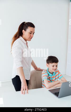 Maman aide son fils à faire des devoirs scolaires sur l'ordinateur Banque D'Images