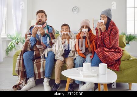 maman malade, papa et enfants assis sur le canapé et éternuant dans des mouchoirs en papier tous ensemble Banque D'Images