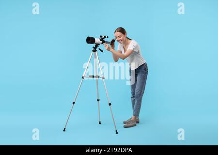 Jeune astronome regardant les étoiles à travers le télescope sur fond bleu clair Banque D'Images