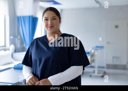 Portrait d'une femme biraciale heureuse médecin dans une chambre d'hôpital ensoleillée Banque D'Images