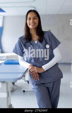 Portrait d'une femme biraciale heureuse médecin dans une chambre d'hôpital ensoleillée Banque D'Images