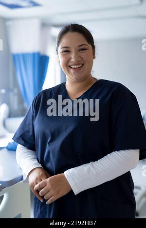 Portrait d'une femme biraciale heureuse médecin dans une chambre d'hôpital ensoleillée Banque D'Images