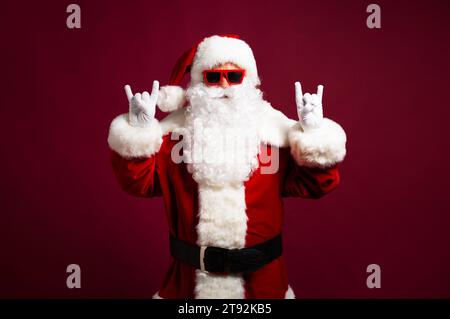 Excité heureux hipster Père Noël dans les écouteurs et les lunettes de soleil s'amuse sur la fête isolé sur un fond rouge Banque D'Images