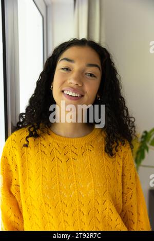 Portrait de femme biracial heureuse en chandail jaune à la maison Banque D'Images