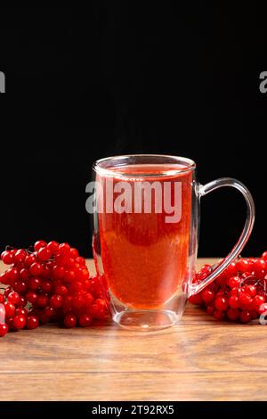 Thé viburnum chaud dans une tasse en verre avec un double fond sur un fond noir. Banque D'Images