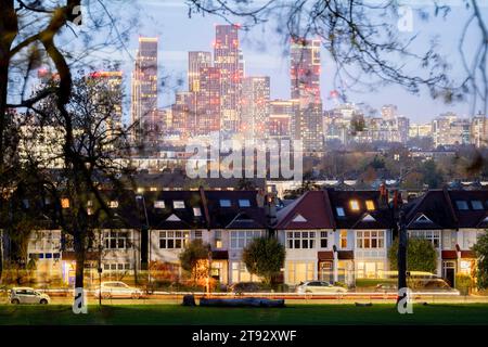 Vu à travers les branches des arbres dans Ruskin Park sont les porches éclairés des maisons d'époque en terrasses et au loin, le développement croissant à Nine Elms à Battersea, le 21 novembre 2023, à Londres, en Angleterre. Banque D'Images