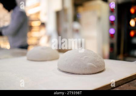 Vue détaillée d'une pâte à pain sur une surface en bois avec un boulanger en arrière-plan d'une boulangerie Banque D'Images