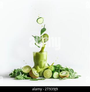 Éclaboussures de smoothie vert dans le verre avec et des ingrédients volants : concombre, kiwi et feuilles d'épinards sur fond blanc avec tas de fruits verts et ve Banque D'Images