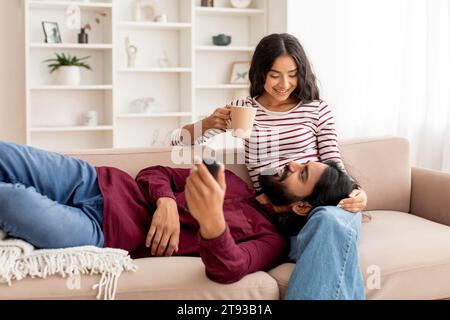 Joyeux jeune indien homme et femme buvant du thé, regardant un film Banque D'Images