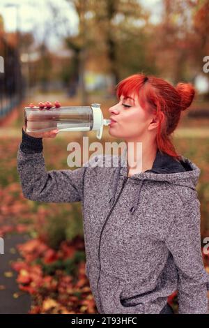 Readhead femme buvant de l'eau de la bouteille dans le parc après l'entraînement Banque D'Images