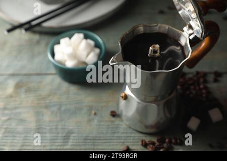 Café infusé dans un pot de moka, des haricots et des cubes de sucre sur une table en bois rustique, closeup. Espace pour le texte Banque D'Images