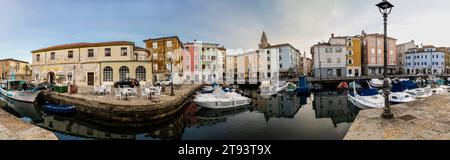 Muggia, Italie – 18 novembre 2023. Vue panoramique du vieux port de Muggia, une ville côtière dans le nord de l'Italie près de Trieste avec un petit moteur amarré Banque D'Images