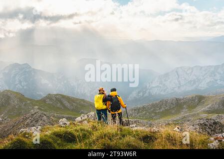 Couple de randonneurs avec des sacs à dos, debout et embrassant au sommet d'une montagne contemplant le paysage de la chaîne de montagnes. sports et plein air Banque D'Images