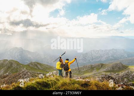 Couple de randonneurs avec des sacs à dos élevant leurs bâtons de trekking alors qu'ils atteignent le sommet d'une montagne. alpinistes contemplant le paysage du moun Banque D'Images