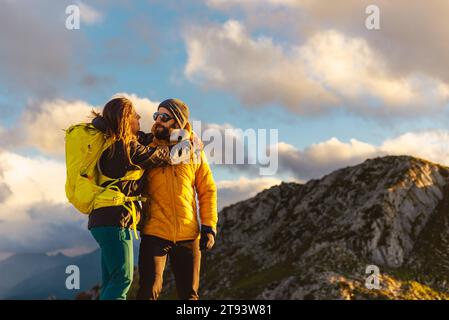 couple d'alpinistes amoureux s'embrassent au sommet d'une montagne au coucher du soleil. randonneurs avec des sacs à dos en plein pic. Banque D'Images