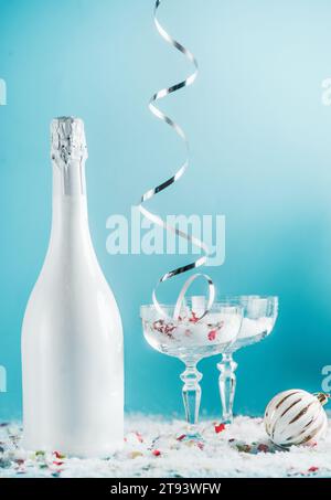 Noël et nouvel an avec bouteille de champagne, verres, ruban argenté tombant, neige et boule et sur fond bleu clair. Vue avant Banque D'Images