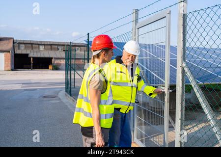 Deux ingénieurs en gilets haute visibilité inspectent un champ de panneaux solaires entrant sur une porte d'installation Banque D'Images