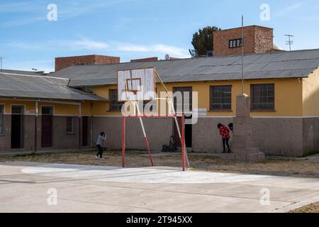 Les enfants jouent dans une cour d'école avec basket ball court et Yellow Buildings Banque D'Images