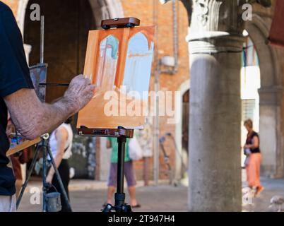 Gros plan de la main d'un peintre alors qu'il peint au pinceau sur toile une scène en plein air dans une petite place à Venise, en Italie Banque D'Images