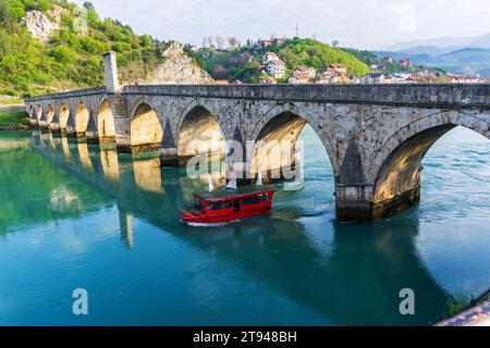 Le bateau touristique passe sous le célèbre pont sur la rivière Drina à Visegrad, en Bosnie-Herzégovine. Banque D'Images