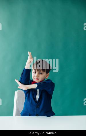 Garçon élève écolier lève la main pour répondre en classe à Desk Education Knowledge Banque D'Images