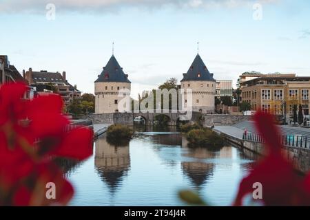 Centre-ville de Kortrijk avec deux tours historiques au bord de la rivière. Fleurs, rivière et bâtiments historiques. Ville belge dans le sud du pays. Banque D'Images