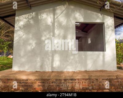 La lumière du coucher de soleil projette les ombres de quelques arbres sur le mur blanc d’un atelier dans une ferme près de la ville d’Arcabuco, dans le centre de la Colombie. Banque D'Images