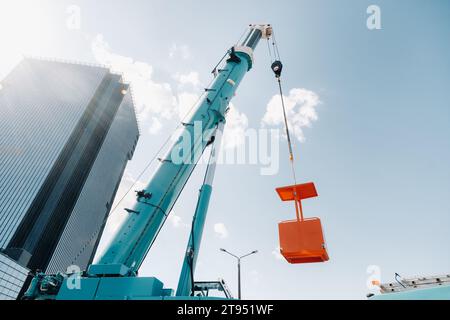 Une grande grue de camion bleue est prête à fonctionner sur un site près d'un grand bâtiment moderne. La plus grande grue de camion avec un berceau jaune pour résoudre c Banque D'Images