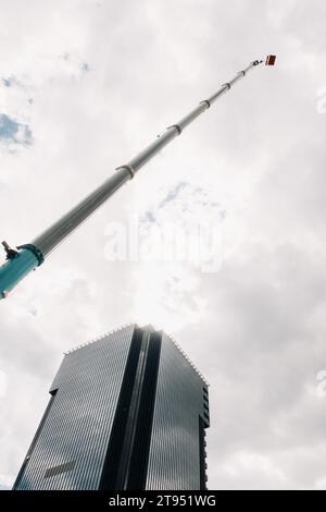 Une grande grue de camion bleue est prête à fonctionner sur un site près d'un grand bâtiment moderne. La plus grande grue de camion avec un berceau jaune pour résoudre c Banque D'Images