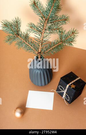 Branche d'épicéa dans un vase en céramique, boîte cadeau et carte vierge sur table beige. Concept de Noël minimal. Vue de dessus, maquette Banque D'Images