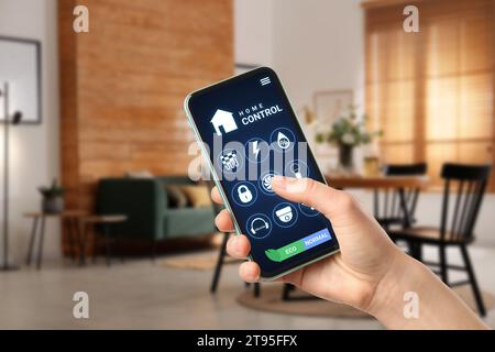 Femme utilisant le système intelligent de contrôle de la maison via l'application sur le téléphone mobile à l'intérieur, closeup Banque D'Images