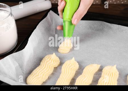 Faire des eclairs. Femme pressant la pâte crue du sac à pâtisserie sur la plaque de cuisson à la table, gros plan Banque D'Images