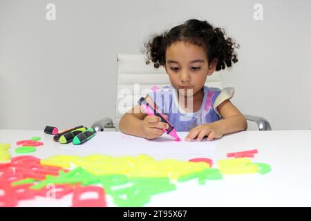 Fille Latina de 3 ans avec les cheveux bruns bouclés dessine comme un outil de thérapie pour le traitement du trouble du spectre autistique TSA et du déficit de l'attention TDAH Banque D'Images