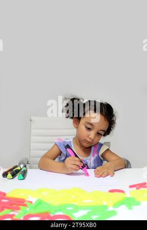 Fille Latina de 3 ans avec les cheveux bruns bouclés dessine comme un outil de thérapie pour le traitement du trouble du spectre autistique TSA et du déficit de l'attention TDAH Banque D'Images